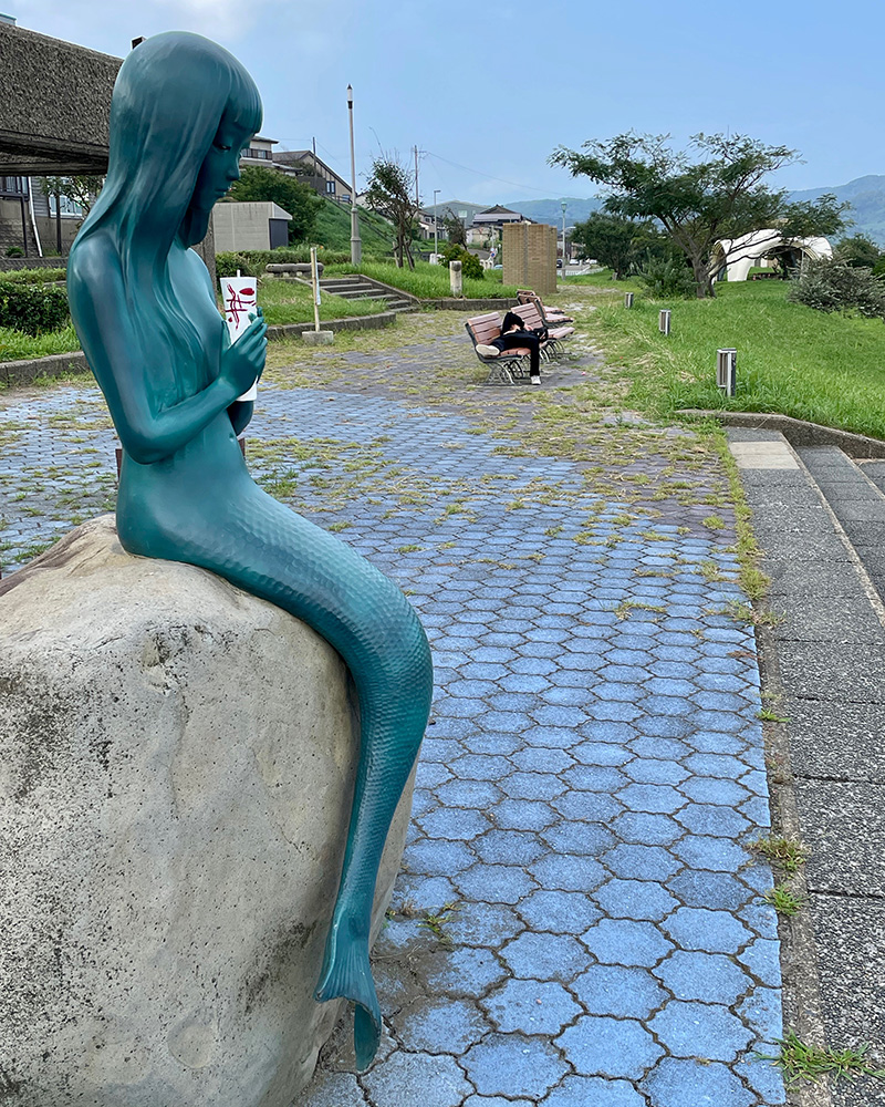 「赤いろうそくと人魚」像と眠る若者の写真